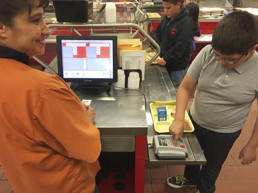 In this Thursday, May 4, 2017 photo, Cafeteria worker Paula Herrera, left, supervises as second grade student Dylan Casias punches in his student identification number to deduct a meal payment at Gonzales Community School in Santa Fe, N.M. All students are offered the same lunch at Gonzales and other Santa Fe public schools to avoid any chance of embarrassing students whose parents may have fallen behind on meal payments. New Mexico in April became the first state to outlaw the shaming of children for any unpaid meals. (AP Photo/Morgan Lee)