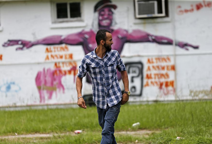 In this June 27, 2017 photo, Abdullah Muflahi walks outside his Triple S Food mart in front of a mural of Alton Sterling in Baton Rouge, La. Little has changed in this poverty-stricken neighborhood since Sterling was shot by police one year ago, a frustrating fact of life for residents and business owners who had hoped a national spotlight on their problems could erode racial tensions and improve police relations in Louisiana's capital. (AP Photo/Gerald Herbert)
