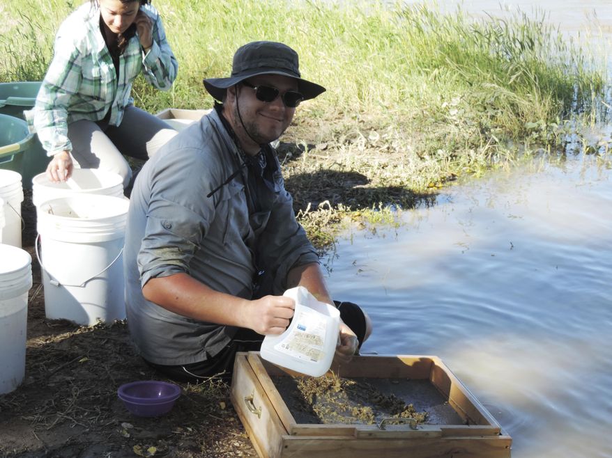 ADVANCE FOR WEDNESDAY JULY 5 AND THEREAFTER - In a June 22, 2017 photo, Lauren Gonzales makes a dirt slurry while David Birlenbach pours an already prepared slurry onto the screens to wash the dirt, in hopes of finding fossils, gathered from an area about 10 miles east of Worland, Wyo., at the Worland Riverside Rotary Park. (Tracie Mitchell/Northern Wyoming Daily News via AP)