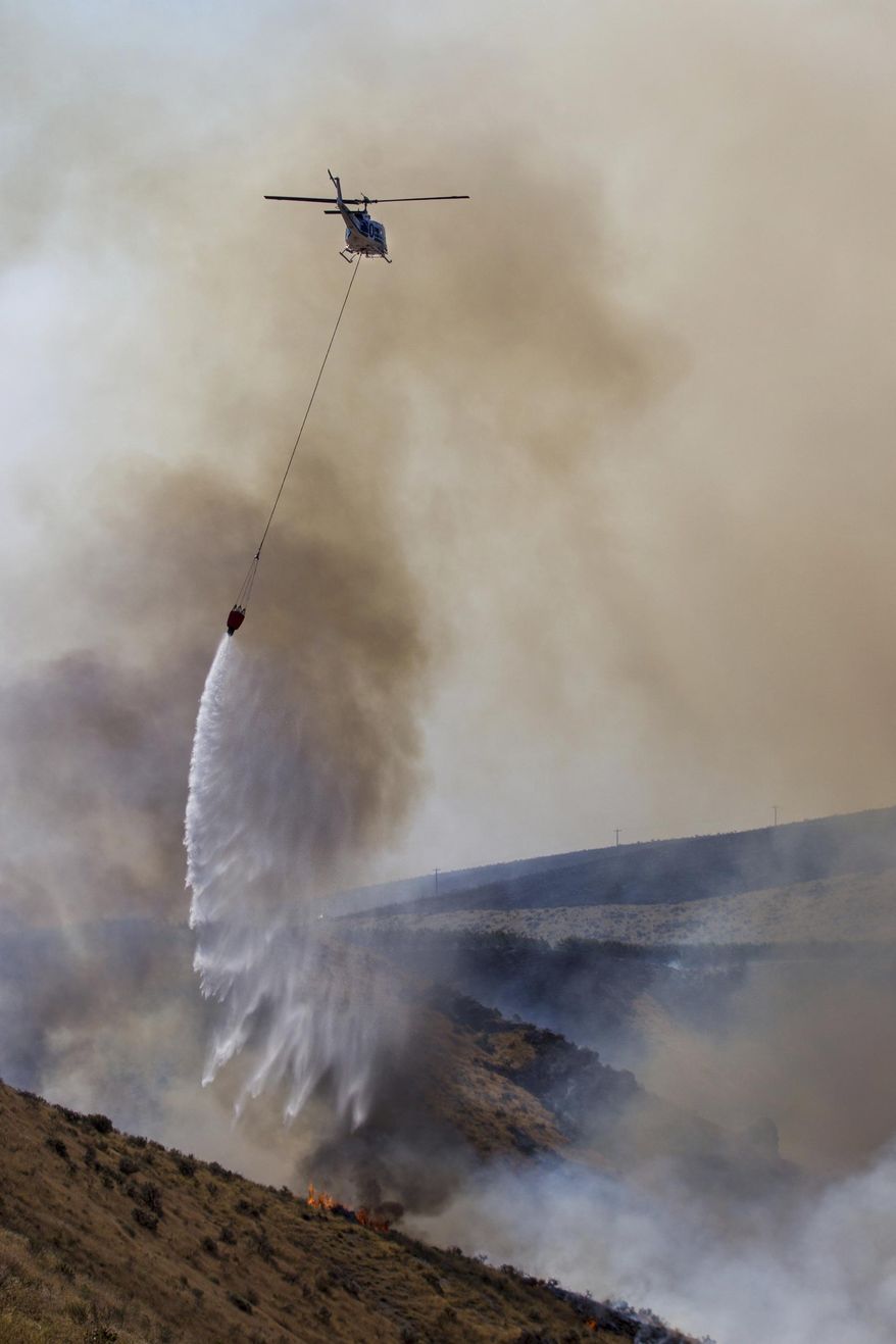 A helicopter dumps water along the fire line as the fire moves down Rattlesnake Ridge in Moxee, Wash., on Thursday, July 6, 2017. The fire burned more than 5,500 acres of mostly grass and brush in less than 24 hours, and threatened about 30 homes. (Jake Parrish/Yakima Herald-Republic via AP)