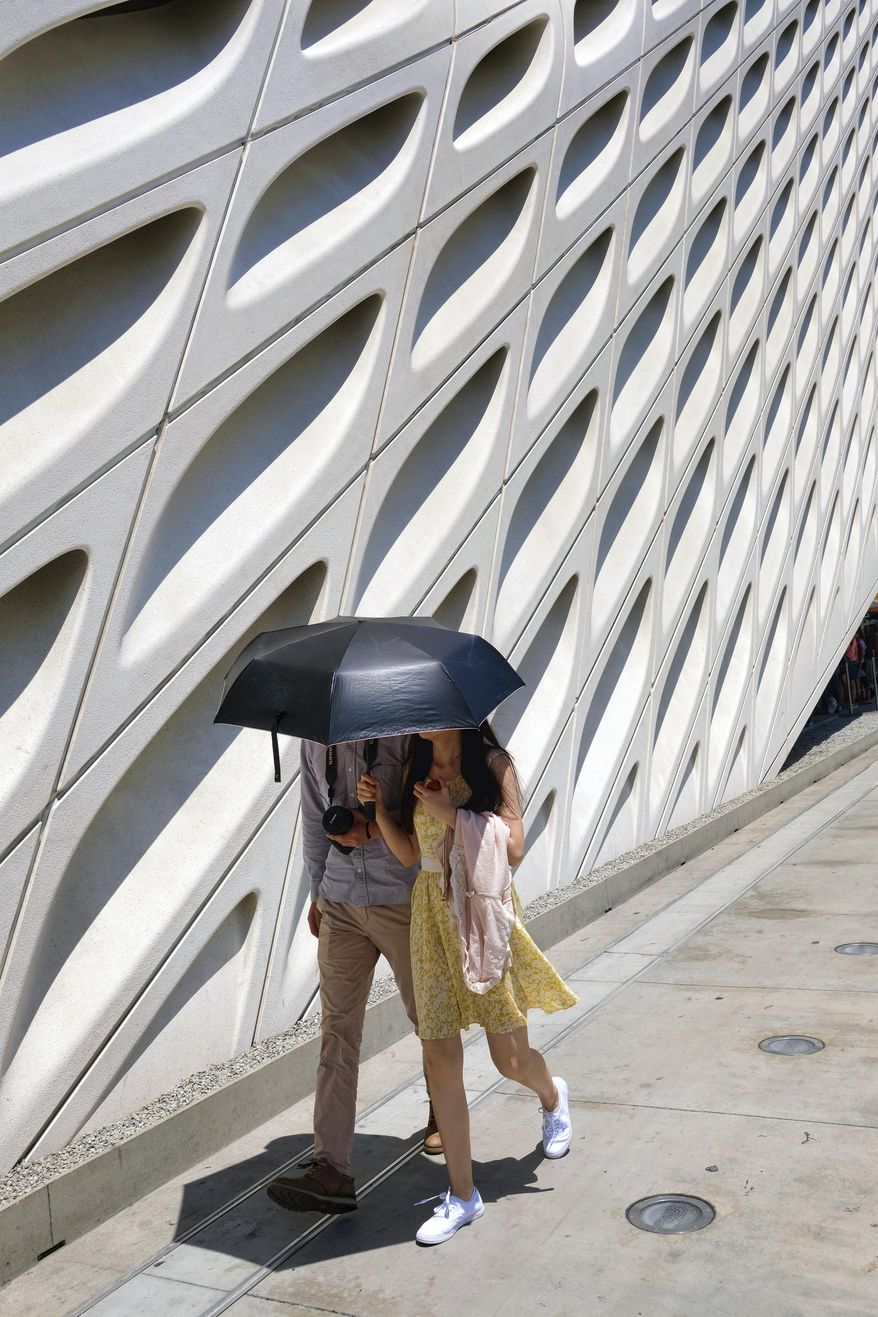 Tourists walking past The Broad Museum while they shade themselves from the afternoon sun in downtown Los Angeles on Friday, July 7, 2017. Southern California faces more blistering heat as firefighters around the state work to corral wildfires. The National Weather Service says high temperatures between 100 and 110 degrees will be common away from the coast Friday and Saturday while some coastal sections could see highs into the 90s. (AP Photo/Richard Vogel)