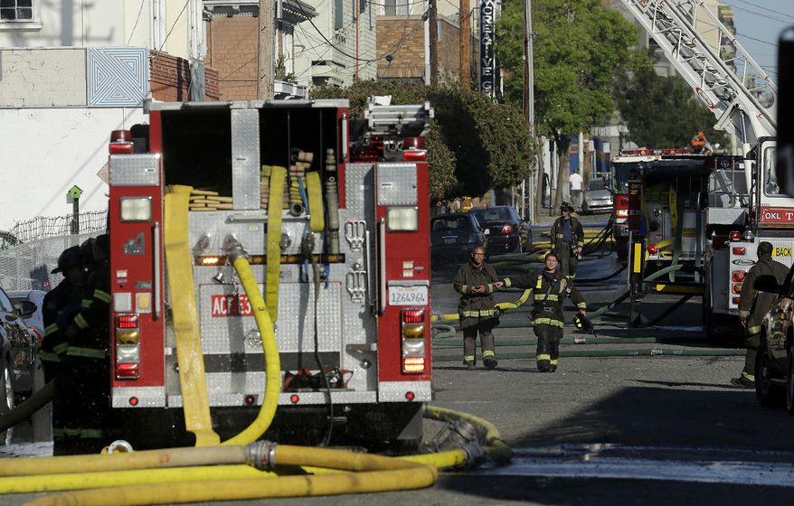 Firefighters walk in front of the scene of a fire in Oakland, Calif., Friday, July 7, 2017. A huge fire at a building under construction in Oakland has been contained early Friday, but evacuations remain in place at nearby buildings. (AP Photo/Jeff Chiu)