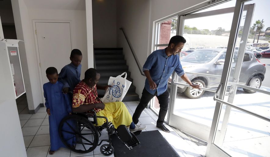 Ali Said, of Somalia, center, leaves a center for refugees with his two sons, as refugee caseworker Mohamed Yassin, right, holds open the door Thursday, July 6, 2017, in San Diego. Said, whose leg was blown off by a grenade, says he feels unbelievably lucky to be among the last refugees allowed into the United States before stricter rules kick in as part of the Trump administration's travel ban. (AP Photo/Gregory Bull)