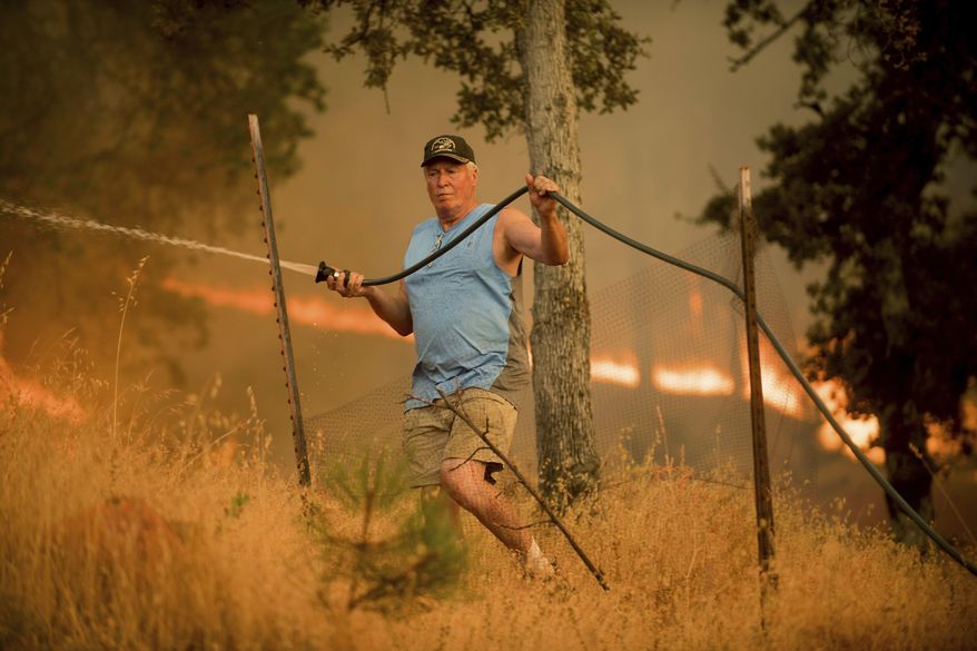 Jim Berglund sprays water while defending his home as a wildfire approaches on Saturday, July 8, 2017, near Oroville, Calif. Although flames leveled Berglund's barn, his home remained unscathed as the main fire head passed. (AP Photo/Noah Berger)