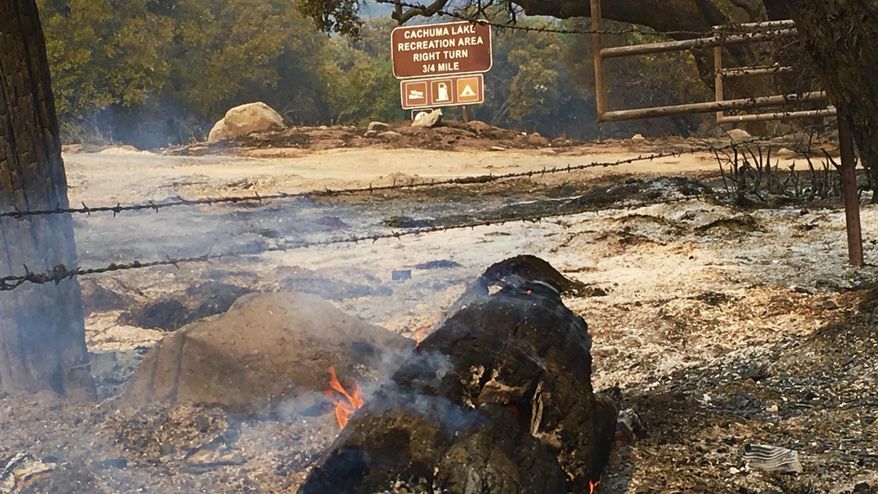This photo provided by KEYT-TV shows the smoldering entrance to a campground at Cachuma Lake after a wildfire swept through in Santa Barbara County, Calif., Sunday, July 9, 2017. Wildfires barreled across the baking landscape of the western U.S. and Canada, destroying a smattering of homes and forcing thousands to flee. Southern California crews hope slightly cooler temperatures and diminishing winds will help in the battle Sunday. (John Palminteri/KEYT-TV via AP)