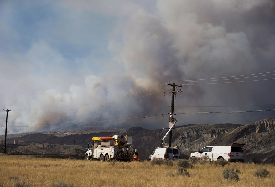 Workers repair power and telecommunication lines damaged by wildfire as a fire burns on a mountain near Ashcroft, British Columbia, Sunday, July 9, 2017. Wildfires barreled across the baking landscape of the western U.S. and Canada, destroying a smattering of homes and forcing thousands to flee. (Darryl Dyck /The Canadian Press via AP)