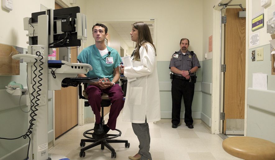 In this Thursday, July 6, 2017, file photo, security officer John Christiansen, right, stands on duty as nursing assistant Jared McCullough, left, and clinical nurse leader Nicole McWhorter, center, discuss a patient in the psychiatric hall of the Dartmouth-Hitchcock Medical Center emergency department in Lebanon, N.H. The emergency department has one security officer assigned to the waiting area, and another assigned to the psychiatric hall with its three patient rooms and a fourth &quot;quiet room.&quot; (James M. Patterson/The Valley News via AP)