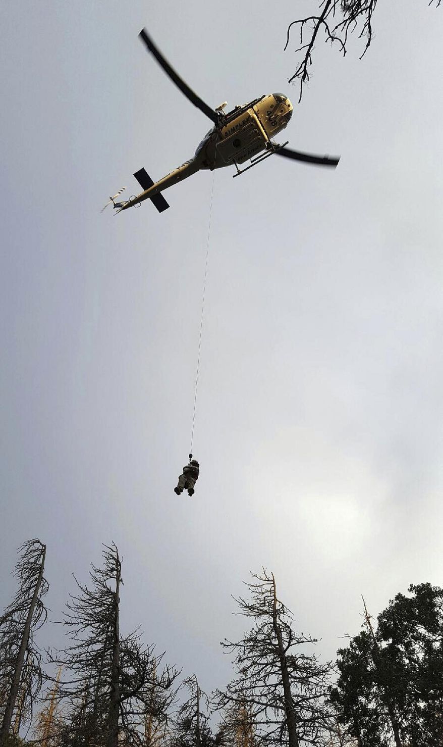 This July 8, 2017 photo provided by Charles Brandenburg shows a Kern County SWAT officer being lowered to help Brandenburg and three hikers on the Pacific Crest Trail near Tehachapi, Calif. The hikers were airlifted to safety after a search and rescue team that was hiking to bring Brandenburg water was robbed at gunpoint by two men. Authorities said an operation to find the culprits was underway Monday, July 10, 2017, in the Piute Mountains about 85 miles north of Los Angeles. (Charles Brandenburg via AP)
