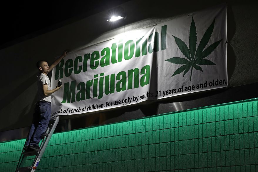 In this June 30, 2017, file photo, Bryce Tallitsch hangs up a sign for recreational marijuana at the NuLeaf dispensary in Las Vegas. (AP Photo/John Locher, File)