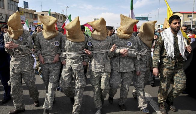 FILE - In this Feb. 11, 2016 file photo, members of the Iranian Basij paramilitary force reenact the January 2016 capture of U.S sailors by the Revolutionary Guard in the Persian Gulf, in a rally commemorating the 37th anniversary of Islamic Revolution, in Tehran, Iran. Mohsen Dehnavi, an Iranian cancer researcher who was denied entry to the U.S. previously headed a student branch of a volunteer paramilitary militia, footage aired on state television Thursday, July 13, 2017, showed. In comments to the channel at the Tehran airport, he defended his travel to the United States as solely intended for science and research. (AP Photo/Ebrahim Noroozi, File)