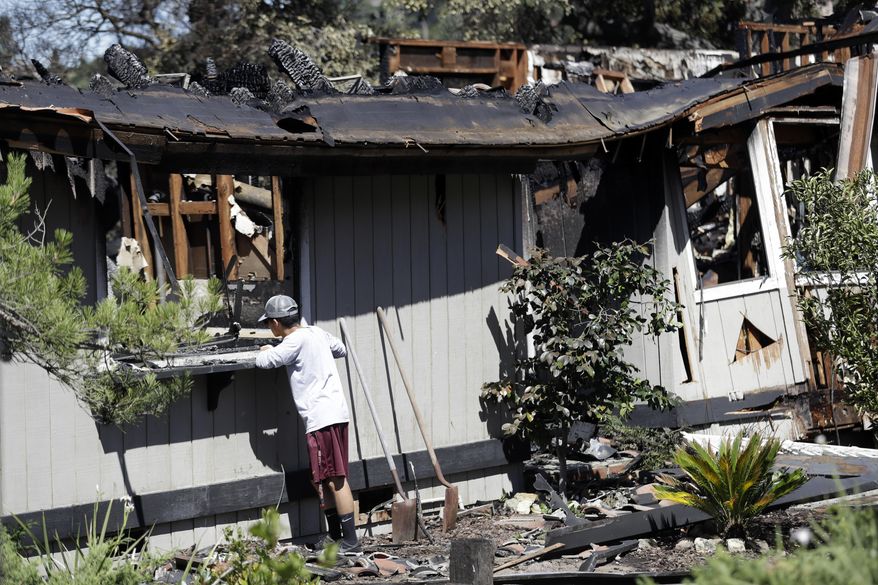 A resident, wishing not to be identified, looks inside a fire ravaged home Wednesday, July 12, 2017, in San Jose, Calif. Relief was arriving after a rough stretch of wildfires all around the U.S. West, with firefighters slowly surrounding once-fierce blazes and evacuees starting to stream back home. (AP Photo/Marcio Jose Sanchez)