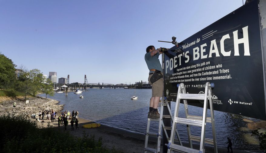 In this Thursday, July 6, 2017 photo, Curt Ellsworth puts up a sign at a section of newly formed beach, named Poet's Beach, on the Willamette River in downtown Portland, Ore. Portland is well-known as a tree-hugging, outdoorsy city, but the river that powers through its downtown has never been part of that green reputation. For decades, residents have been repulsed by the idea of swimming in the Willamette River because of weekly sewage overflows that created a bacterial stew. Now, the recent completion of a $1.4 billion sewage pipe has flushed those worries - and the river once shunned by swimmers is enjoying a rapid renaissance. (AP Photo/Don Ryan)