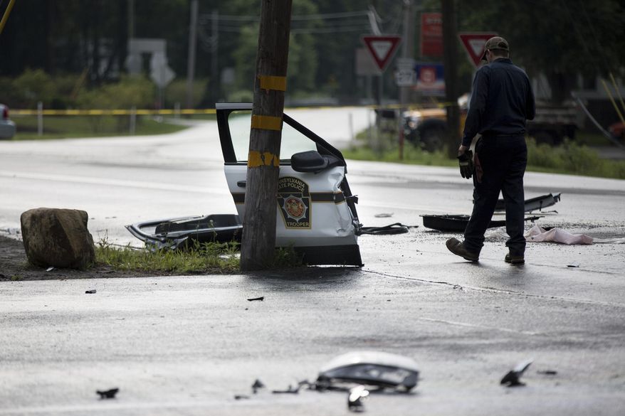 A tow truck operator makes a phone call amid the wreckage after a Pennsylvania State Trooper vehicle and garbage truck collided in Ligonier Township, Pa., Friday, July 14, 2017. A state trooper died and another was injured in the crash. The conditions of the injured trooper and the garbage truck driver were not immediately known (Alex Driehaus//Pittsburgh Post-Gazette via AP)