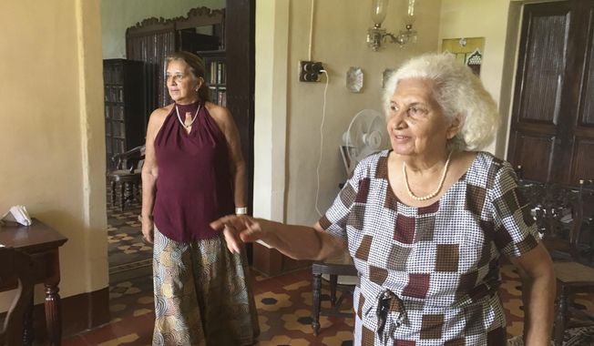 In this Friday June 2, 2017 photo, Maria de Lourdes Figueiredo de Albuquerque, 87, right, and her daughter Maria de Fatima Figueiredo de Albuquerque walk in one of the rooms of their 427-year-old Portuguese heritage home in Goa, India. The home is a much-loved and lived-in repository of memories tracing to when what is now the west-coast Indian state of Goa was a Portuguese colony. Far from the party beaches and liquor shacks that Goa has become known for, the mansion is now open as both a homestay and a museum, filled with antique furniture and artifacts from the 17th century. (AP Photo/Manish Mehta)
