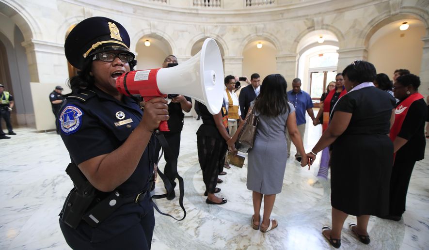 A U.S. Capitol Police officer gives the warning speaking through a bullhorn to a group of Black minister gathered to protest on Capitol Hill in Washington, Tuesday, July 18, 2017, demanding Congress to "reject both the immoral budget proposed by the Trump Administration and the equally unjust health care bill that the Senate may have a procedural vote on in the coming weeks." (AP Photo/Manuel Balce Ceneta)
