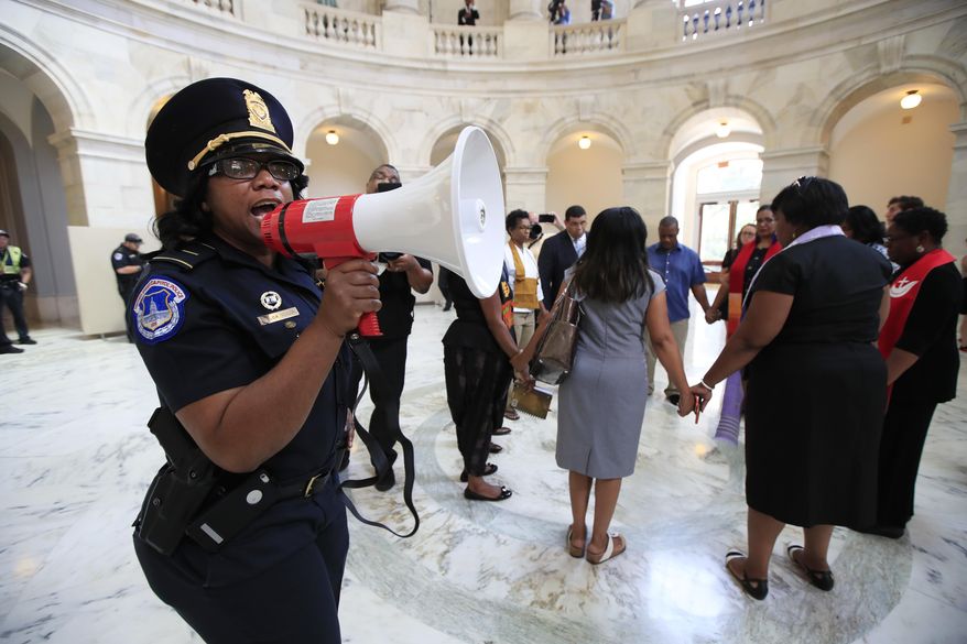 A U.S. Capitol Police officer gives the warning speaking through a bullhorn to a group of Black minister gathered to protest on Capitol Hill in Washington, Tuesday, July 18, 2017, demanding Congress to "reject both the immoral budget proposed by the Trump Administration and the equally unjust health care bill that the Senate may have a procedural vote on in the coming weeks." (AP Photo/Manuel Balce Ceneta)