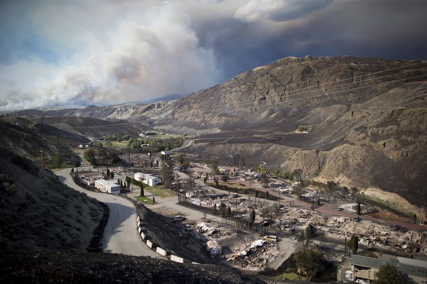 The remains of mobile homes destroyed by a wildfire are seen in Boston Flats as a fire burns on a mountain near Ashcroft, British Columbia, Canada, on Sunday, July 9, 2017. California officials said the extraordinarily wet winter caused thick spring blooms that are now dried out and burning, making for unpredictable fire behavior. (Darryl Dyck/The Canadian Press via AP)