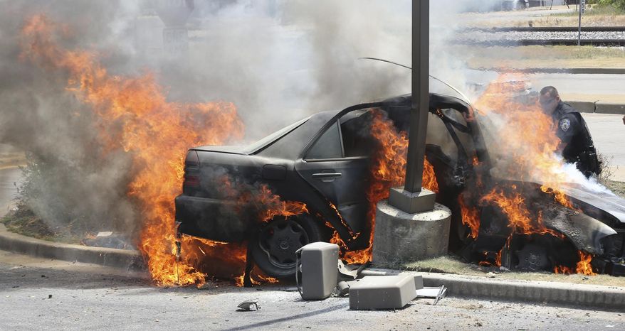 Alton police officer Ryan Parker uses a fire extinguisher to try to slow the flames engulfing a car that crashed Thursday July 20, 2017, in Alton, Ill., as two people are inside. Firefighters were able to pull the driver free, but both occupants were flown to a St. Louis hospital. (John Badman/The Telegraph via AP)