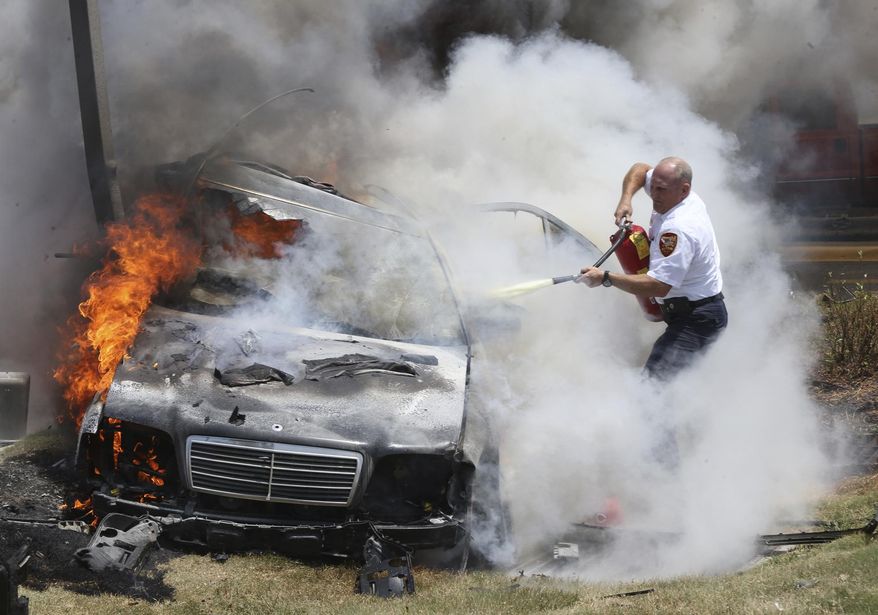 Alton Fire Chief Bernie Sebold, who arrived ahead of his equipment, uses a fire extinguisher to try and reach the driver of car that crashed Thursday July 20, 2017, in Alton, Ill., as flames engulf the vehicle. Firefighters were able to pull the driver free, but both occupants were flown to a St. Louis hospital. (John Badman/The Telegraph via AP)