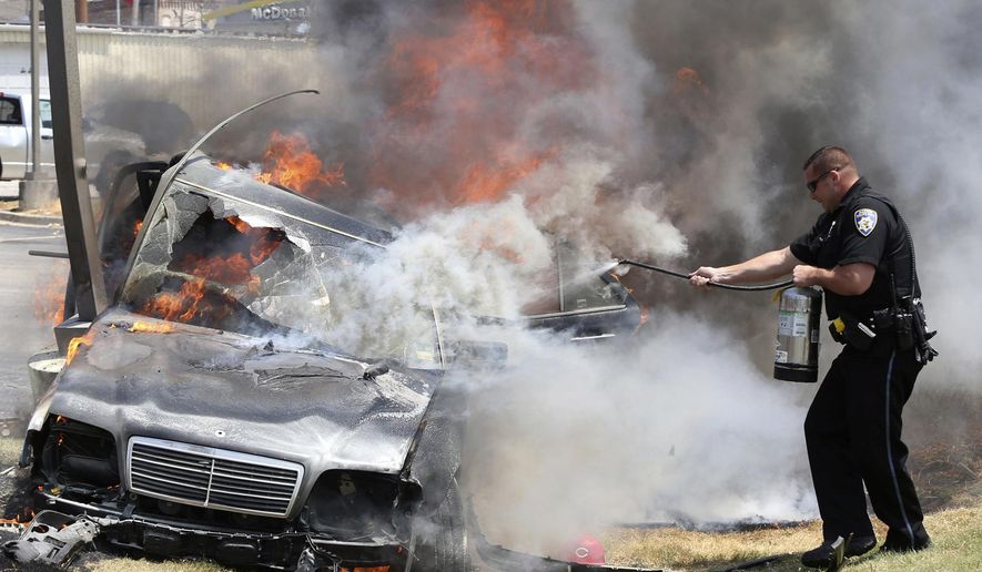 Alton police officer Ryan Parker uses a fire extinguisher to try to slow the flames engulfing a car that crashed Thursday July 20, 2017, in Alton, Ill., as two people are inside. Firefighters were able to pull the driver free, but both occupants were flown to a St. Louis hospital. (John Badman/The Telegraph via AP)