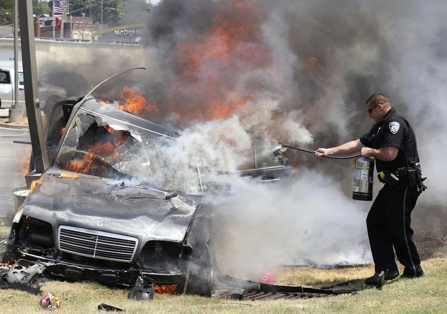 Alton police officer Ryan Parker uses a fire extinguisher to try to slow the flames engulfing a car that crashed Thursday July 20, 2017, in Alton, Ill., as two people are inside. Firefighters were able to pull the driver free, but both occupants were flown to a St. Louis hospital. (John Badman/The Telegraph via AP)