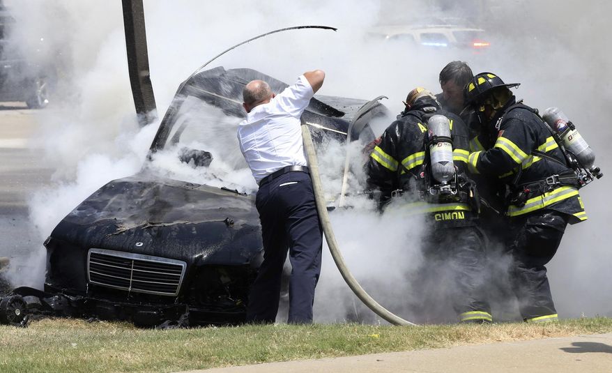 Alton Fire Chief Bernie Sebold, left, pushes a hose into a car after it was engulfed in flames after a crash as firefighters work to free an occupant Thursday July 20, 2017, in Alton, Ill. The occupants of the vehicle were flown to a St. Louis hospital. (John Badman/The Telegraph via AP)