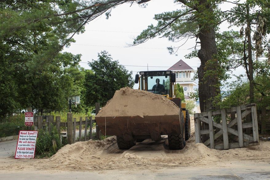 In a July 13, 2017 photo, sand is removed from the location where one cottage was swallowed by an approximately 80-foot tall dune in April at the edge of the Silver Lake Lake State Park in Mears, Mich. There are currently 11 cottages that are in the immediate path of the dune. (Joel Bissell/Muskegon Chronicle via AP)