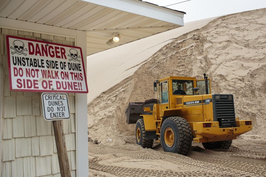 In a July 13, 2017 photo, sand is removed from the location where one cottage was swallowed by an approximately 80-foot tall dune in April at the edge of the Silver Lake Lake State Park in Mears, Mich. There are currently 11 cottages that are in the immediate path of the dune. (Joel Bissell/Muskegon Chronicle via AP)