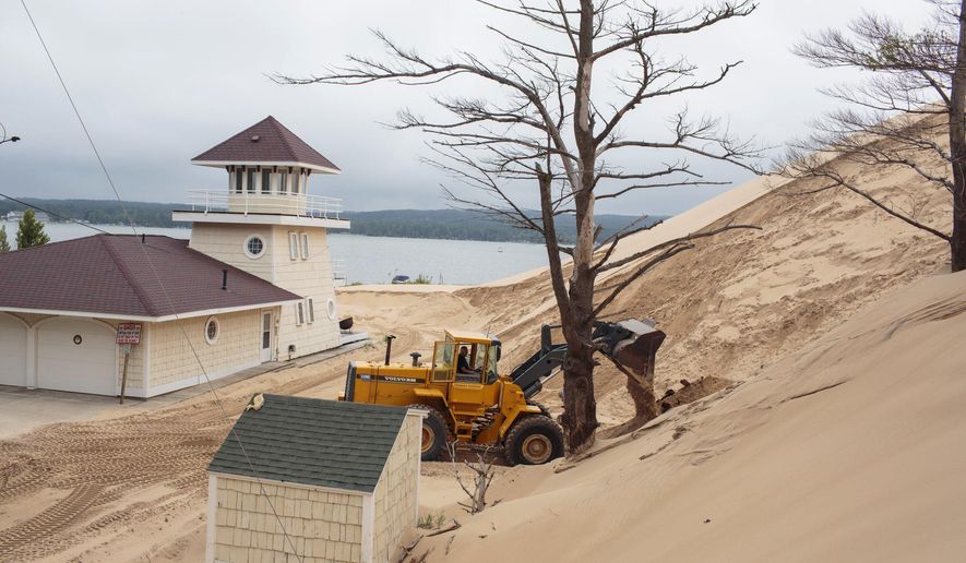 In a July 13, 2017 photo, sand is removed from the location where one cottage was swallowed by an approximately 80-foot tall dune in April at the edge of the Silver Lake Lake State Park in Mears, Mich. There are currently 11 cottages that are in the immediate path of the dune. (Joel Bissell/Muskegon Chronicle via AP)