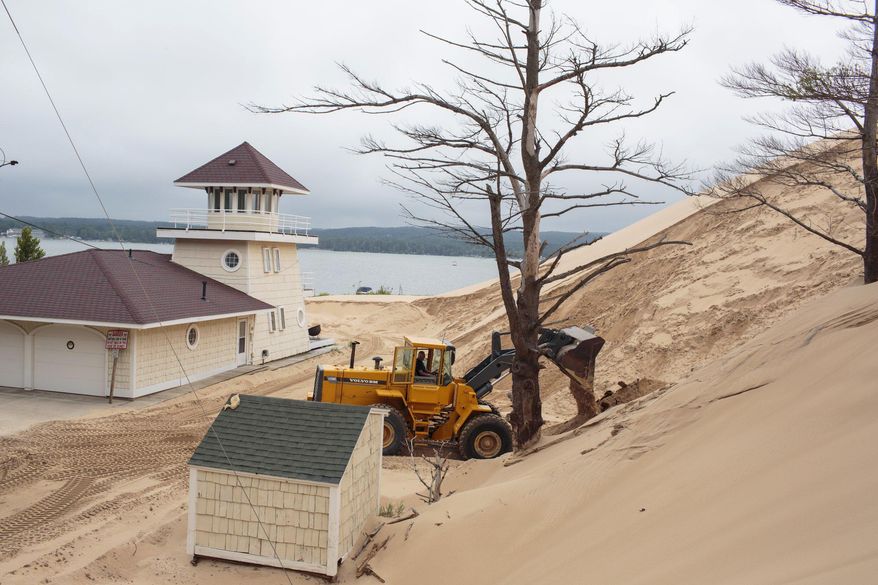 In a July 13, 2017 photo, sand is removed from the location where one cottage was swallowed by an approximately 80-foot tall dune in April at the edge of the Silver Lake Lake State Park in Mears, Mich. There are currently 11 cottages that are in the immediate path of the dune. (Joel Bissell/Muskegon Chronicle via AP)