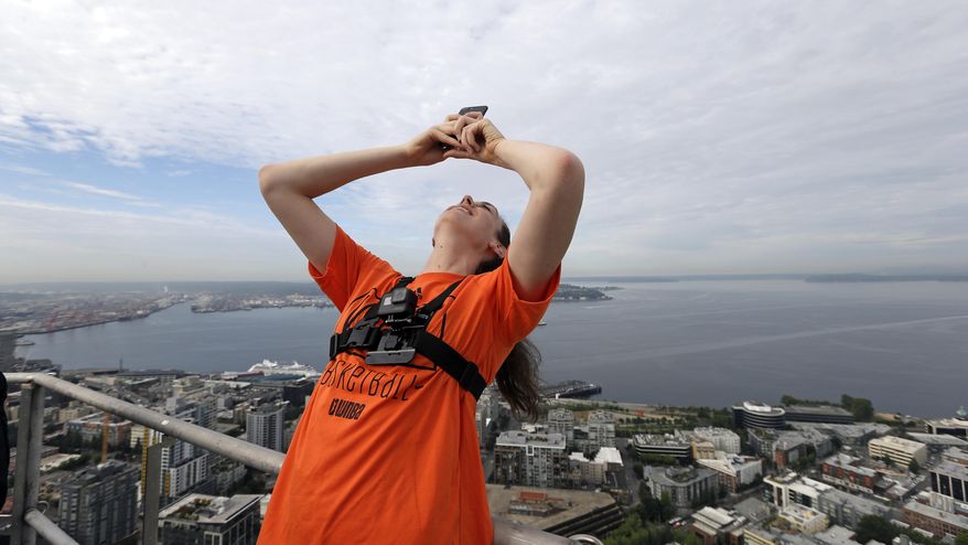 Seattle Storm&#39;s Breanna Stewart, with a camera strapped to her chest to record the day&#39;s activities, leans back from a platform about 575-feet high atop the Space Needle and in view of Elliott Bay before joining other WNBA basketball All-Star players to raise the league flag atop the structure Friday, July 21, 2017, in Seattle. The WNBA All-Star game is Saturday in Seattle. (AP Photo/Elaine Thompson)