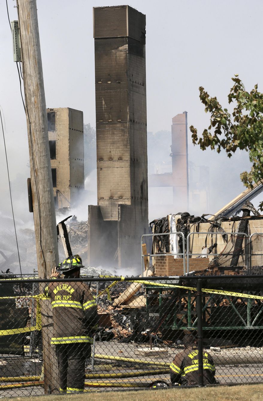 Firefighters pause near the destroyed remains of an under-construction apartment complex, Sunday, July 23, 2017, in Waltham, Mass. Waltham Fire Chief Paul Ciccone says the complex's five buildings collapsed in an early Sunday fire. No injuries have been reported. (AP Photo/Steven Senne)