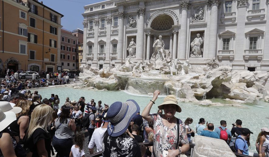 A tourist tosses a coin onto renown Trevi Fountain in Rome, Tuesday, July 25, 2017. Visitors are granted access to the border of the fountain in ordinate and controlled flow, under the supervision of two associations of volunteers, after Rome municipality decided to limit the access to the border of the fountain during an 80 days test period, to avoid excessive crowding and improper behaviors. (AP Photo/Gregorio Borgia)