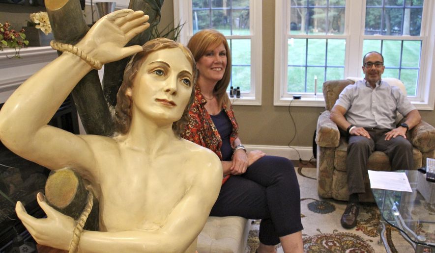 In this June 14, 2017, photo provided by WHYY, Ed and Kathleen Nader sit in their living room in Exton, Pa, with a statue of St. Pantaleon that has been in Ed's family for four generations. The nearly life-sized statue missing for decades from an Italian church is being returned by the American couple, who finally solved the mystery of their family's odd relic. (Emma Lee/WHYY via AP)