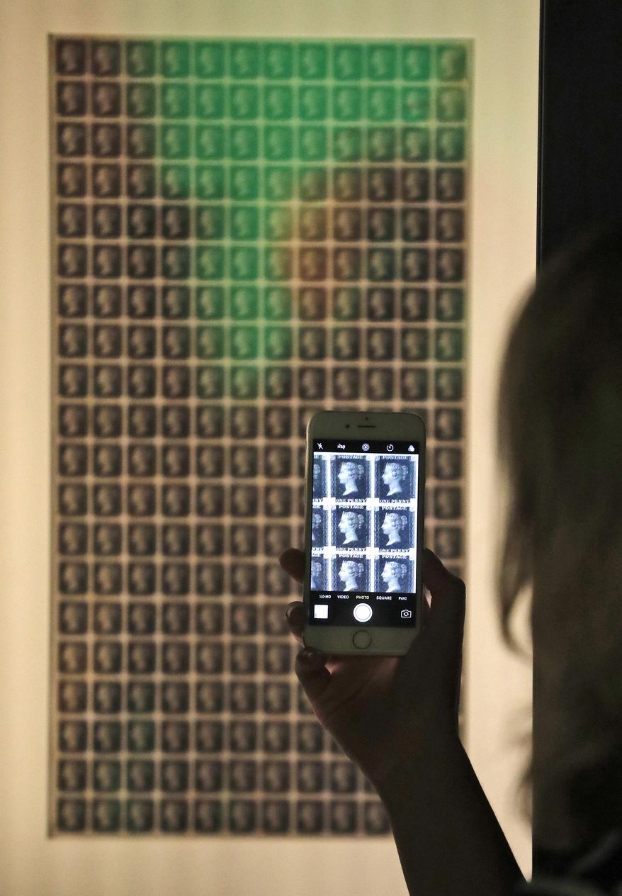 A woman photographs the first Penny Black Proof Sheet at the Postal Museum in London, Wednesday, July 26, 2017. London's newest tourist attraction is perfect for underground explorers. It's not ideal for the claustrophobic. A visit to Mail Rail, a subterranean train network that once carried millions of letters a day across the city, involves a cramped journey through dark tunnels 70 feet (21 meters) below the surface, on a very small train. It's atmospheric, but not roomy. (AP Photo/Frank Augstein)