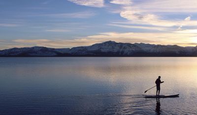 File - In this Feb. 15, 2016, file photo, a stand-up paddleboarder glides across Lake Tahoe at sunset in California. An annual report on Lake Tahoe said the United States&#39; largest alpine lake is still warming at 14 times the historic average. The finding is in the yearly report released Thursday, July 27, 2017, by the University of California at Davis on the state of Lake Tahoe, which straddles the California and Nevada borders. (Claire Cudahy/The Tahoe Tribune via AP, File)