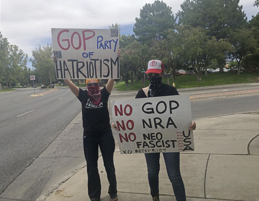 Two protesters who said they from were the activist group Betsy Riot demonstrate outside the offices of the Republican Party of New Mexico in Albuquerque on Thursday, July 17, 2017. New Mexico GOP spokesman Dominic Pacheco said Thursday a receptionist saw the demonstrators paint a red "A'' on a headquarters building sign before fleeing. (AP Photo/Russell Contreras)