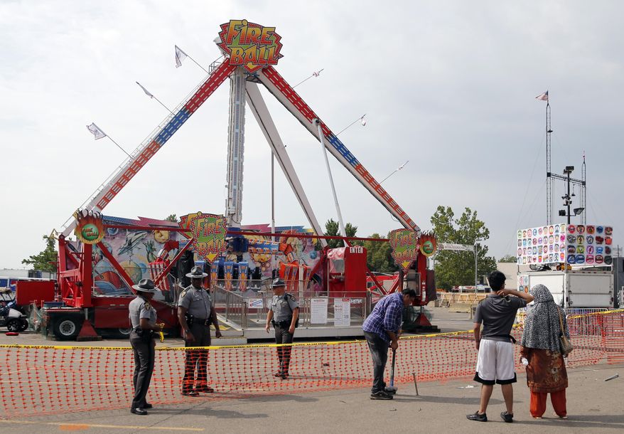Passers by look at the fire ball ride as Ohio State Highway Patrol troopers stand guard at the Ohio State Fair Thursday, July 27, 2017, in Columbus, Ohio. The fair opened Thursday but its amusement rides remained closed one day after Tyler Jarrell, 18, was killed and seven other people were injured when the thrill ride broke apart and flung people into the air. (AP Photo/Jay LaPrete)