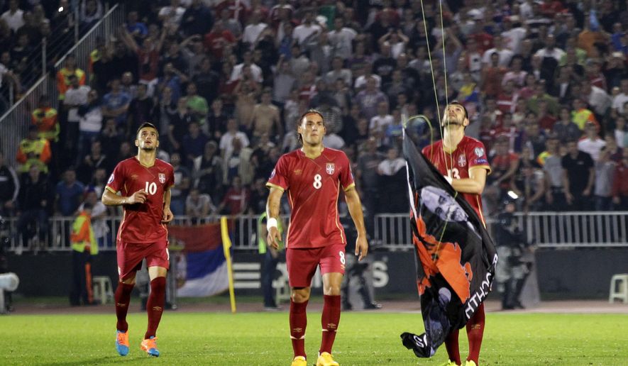 FILE - In this file photo dated Tuesday, Oct. 14, 2014, Serbia&#39;s Stefan Mitrovic grabs a banner containing the Albanian flag attached to a drone flying above the pitch during the Euro 2016 Group I qualifying match between Serbia and Albania in Belgrade, Serbia. The banner prompted fan violence with the match was suspended, and a man who claims to have flown the drone has been detained but it is revealed Saturday July 29, 2017, that Albania’s soccer federation is calling on Albanian authorities to stop his extradition to Serbia. (AP Photo/Darko Vojinovic, FILE)
