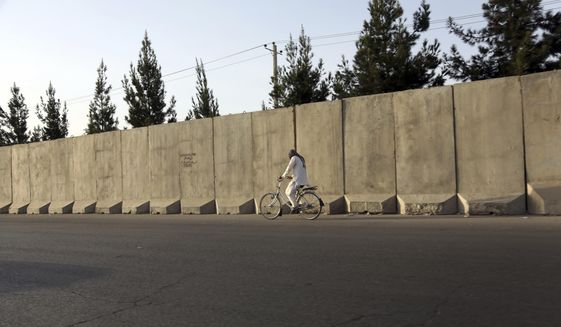 In this Monday, July 31, 2017 photo, an Afghan man ride his bicycle walks past blast walls in Kabul, Afghanistan. A U.S. watchdog says unprecedented security restrictions are making it difficult to monitor Afghanistan projects that are costing hundreds of millions of U.S. tax dollars. (AP Photos/Rahmat Gul)