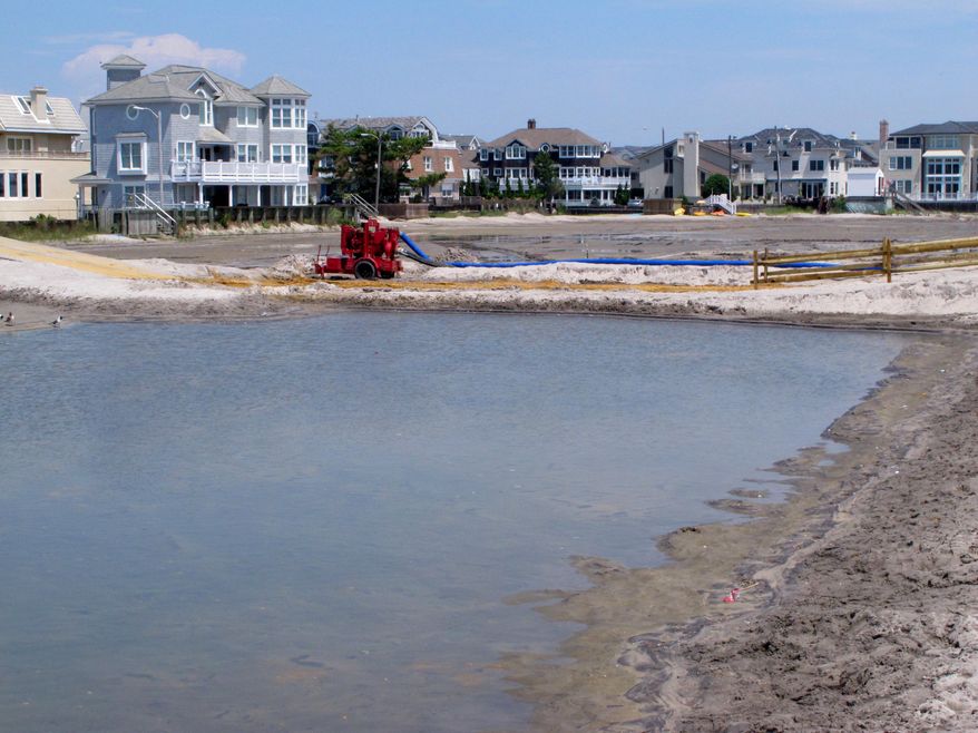 A large pool of water remains on the beach in Margate N.J. on Wednesday Aug. 2, 2017, following weekend rain storms that flooded parts of the beach. A second pond in background is largely empty after having been pumped out into the ocean. On Wednesday, city officials voted to seek a court injunction to halt the construction of sand dunes in the New Jersey shore town, which they blame for the pools. (AP Photo/Wayne Parry)