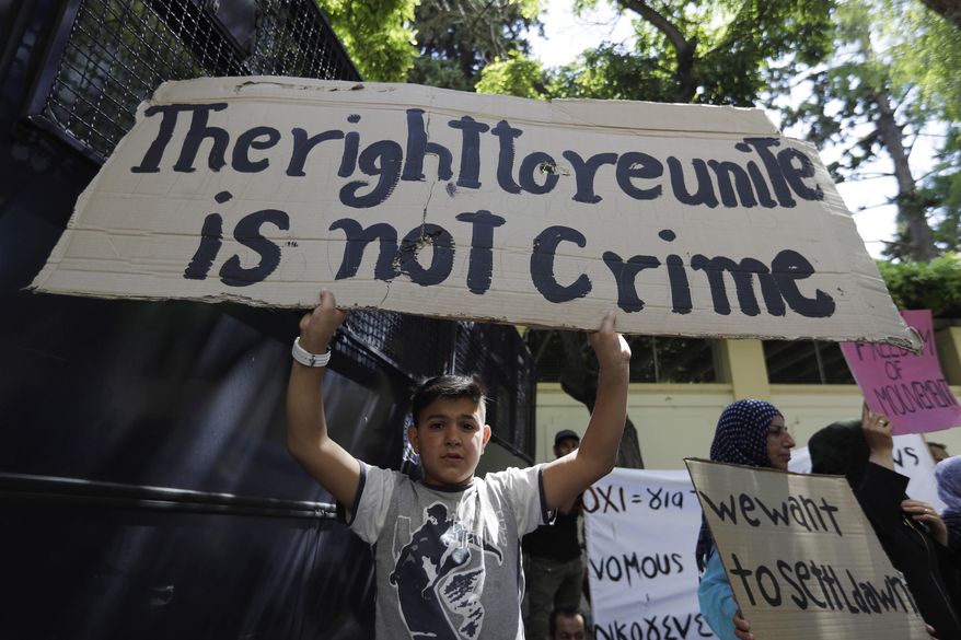 A boy holds up a banner as stranded migrants and refugees gather outside the German Embassy during a protest in Athens, on Wednesday, Aug. 2, 2017. About 150 people, most of them from Syria, marched to protest Germany's decision to limit number of family reunification from Greece. (AP Photo/Thanassis Stavrakis)