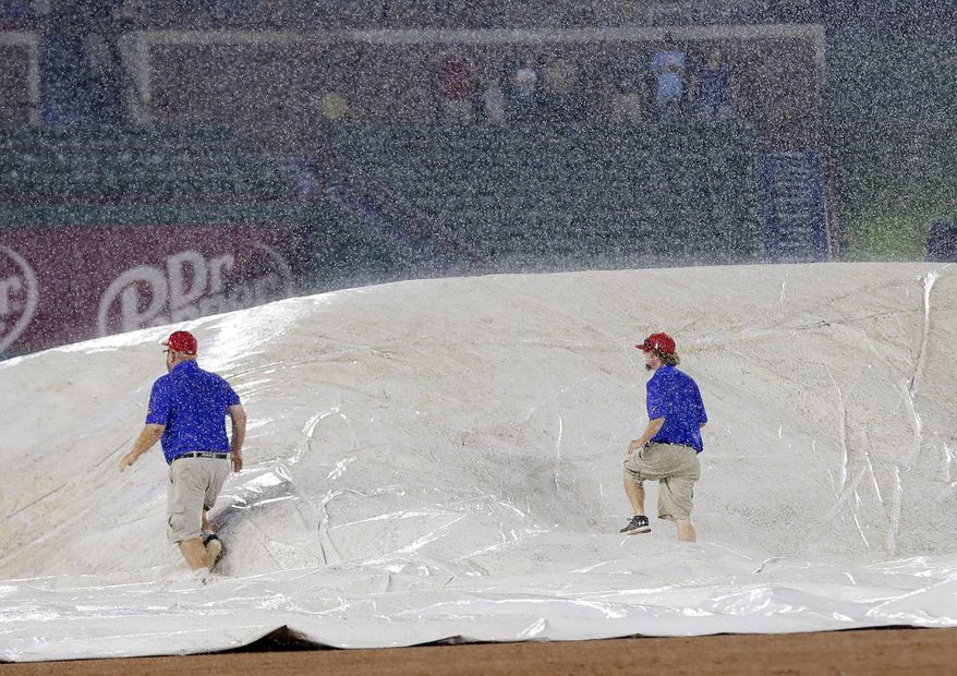 Grounds crew personnel walk over the field tarp trying to remove the air caught beneath as they place it over the field during a heavy rain in the sixth inning of a baseball game between the Seattle Mariners and the Texas Rangers on Wednesday, Aug. 2, 2017, in Arlington, Texas. (AP Photo/Tony Gutierrez)