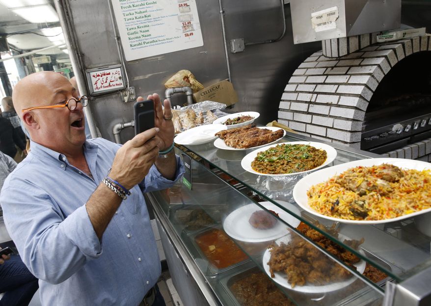 In this Thursday, July 20, 2017 photo, the Travel Channel's "Bizarre Foods" host Andrew Zimmern snaps a cell phone photo of chicken kebabs, far left, a dish composed of organ meats, center, and a goat dish called katakat at Kababish, a Pakistani, Indian and Bangladeshi takeout food shop in the Jackson Heights section of New York. Zimmern says, "I purposely set out to make a show that's entertaining," he said. "At the same time I try to be very thoughtful and thought-provoking and I try to educate and I take the cultural lessons of the show very, very, very seriously." A new show, "The Zimmern List," debuts early 2018 showcasing his favorite places, "where I actually go when the cameras aren't rolling." (AP Photo/Kathy Willens)
