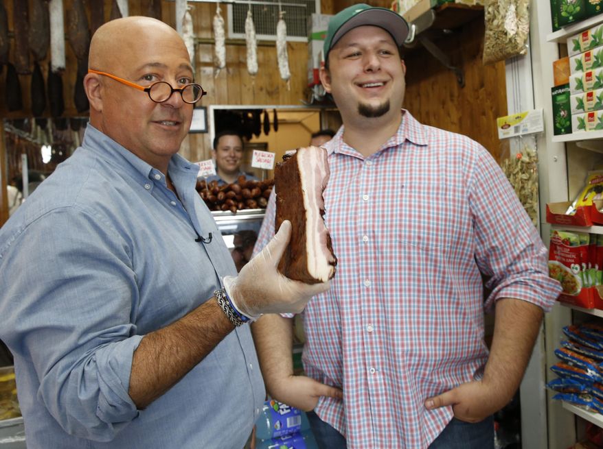 In this photo taken Thursday, July 20, 2017, "Bizarre Foods" host Andrew Zimmern, left, holds a slab of Carska bacon after savoring a small piece of it at Muncan Meats in Astoria, Queens, in New York. Marko Stefanovic, grandson of the store's founder, laughs during the visit. A new show debuting in early 2018, "The Zimmern List," will showcase Zimmern's personal favorites, the eateries where he goes when cameras aren't rolling. (AP Photo/Kathy Willens)