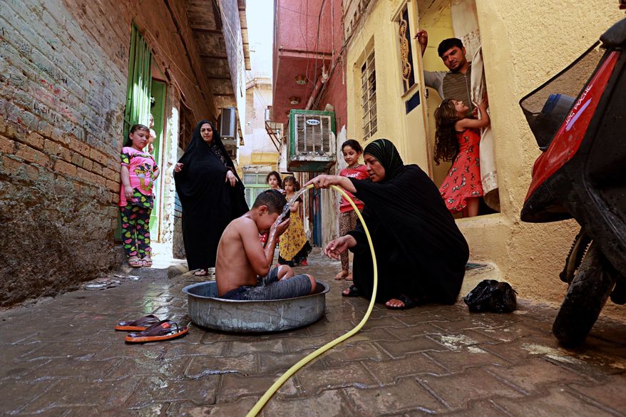 In this photo taken on Friday, July 28, 2017, Umm Ali gives her son a bath to beat the heat in the poor neighborhood of Fadhil in Baghdad, Iraq. Iraq&#39;s weather service warned Thursday that temperatures will increase next week in most parts of the country, with the highs expected to reach 51 degrees Celsius, or about 124 degrees Fahrenheit, adding to the daily woes of Iraqi citizens already facing a deteriorated security situation and lack of public services. (AP Photo/Hadi Mizban)