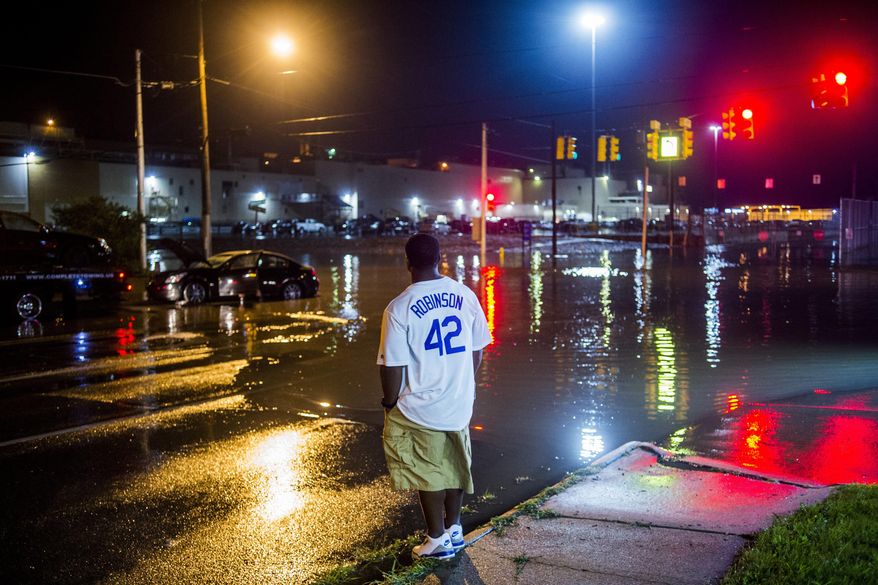 In this Aug. 2, 2017 photo, a Flint, Mich., resident watches as a tow truck driver tries to rescue his car from the flooded roadway in Flint, Mich. The storms Wednesday evening brought several inches of rain in places. (Jake May/The Flint Journal-MLive.com via AP)