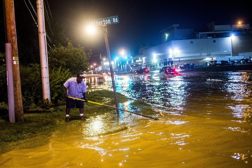 In this Wednesday, Aug. 2, 2017 photo, Entrice Mitchell, a City of Flint sewer department employee, continuously clears debris from an open manhole cover near General Motors Flint Assembly Plant in Flint, Mich. The storms Wednesday evening brought several inches of rain in places. (Jake May/The Flint Journal-MLive.com via AP)