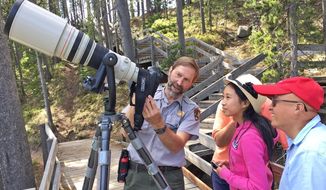In this June 8, 2017 photo, Yellowstone National Park photographer Jim Peaco, left, gives Sunnyvale, Calif., tourists Amanda and Stephen Chou a lesson in shutter speeds while photographing harlequin ducks in the LeHardy Rapids section of the Yellowstone River in Yellowstone National Park, Wyo. From garbage truck driver to seasonal slide librarian in 1984, Peaco finally got a toehold on a dream job: Yellowstone National Park photographer.  (Brett French/The Billings Gazette via AP)