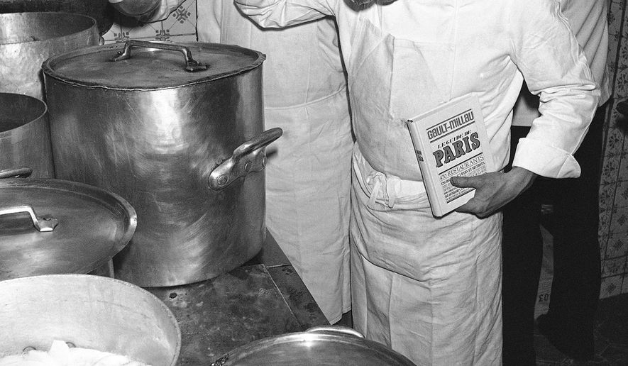 FILE- In this Dec. 5, 1977 file photo, French chefs and restaurant critics Christian Millau, tasting and holding their book, right, with Henri Gault, at left, pose near an oven in a Parisian restaurant in Paris, France at the occasion of the presentation of their new "Gault and Millau" restaurant guide. Millau, who built a renowned French restaurant guide with colleague Gault and was among the originators of the Nouvelle Cuisine food movement in the 1970s, died in Paris over the weekend at 88. (AP Photo/Jacques Langevin, File)